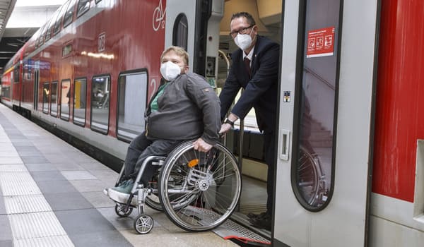Eine Rollstuhlfahrerin steigt in einen Regionalzug ein und wird dabei von einem Bahnbediensteten unterstützt.